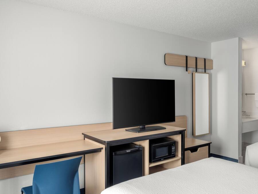 Habitación de hotel con cama, escritorio con televisor de pantalla plana, microondas, basurero pequeño y espejo.
