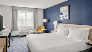 Habitación de hotel con una cama grande, un escritorio, una silla, una mesita de noche, una lámpara y una ventana con cortinas.