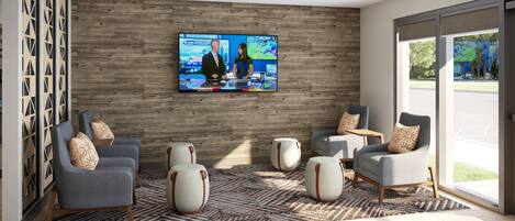 Un interior moderno con un televisor de pantalla plana montado en una pared de madera, dos sillones grises con cojines estampados, un reposapiés blanco redondo y una alfombra con motivos.