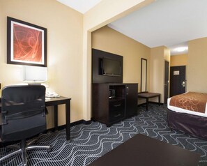 Habitación de hotel con escritorio, silla, televisor, armario, cama y alfombra estampada.