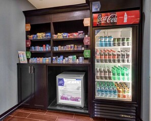 A vending machine stocked with snacks and beverages, a Coca-Cola refrigerator, and a freezer with a 'FROZEN FARE' sign.
