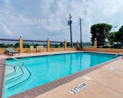 Piscina com espreguiçadeiras e área cercada.