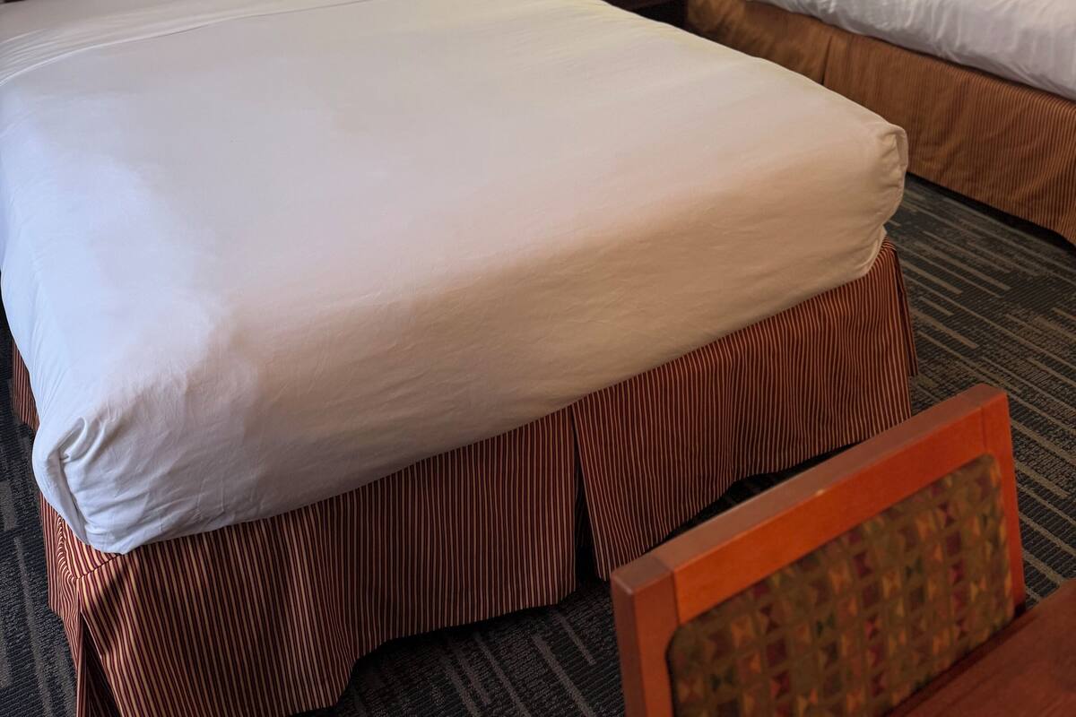 A hotel room with two beds, a nightstand with a lamp, and framed pictures on the wall.