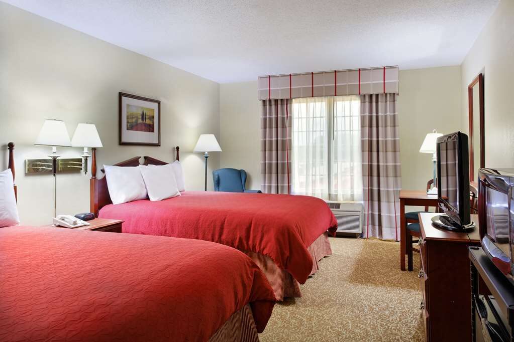 A hotel room with two beds, a television, a desk, and a chair.