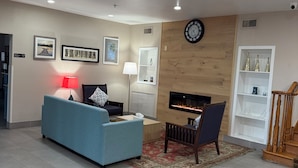A modern living room with a blue sofa, a fireplace, and a clock on the wall. - Country Inn & Suites by Radisson, Elgin, IL (Elgin)
