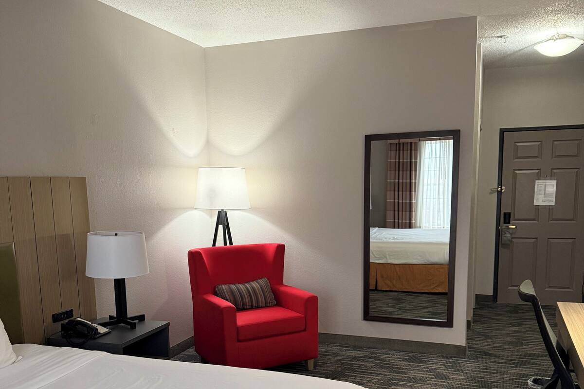 A hotel room with a large bed, a red armchair, a desk, and a mirror.