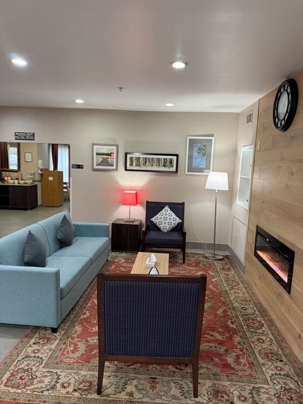A living room with a blue sofa, a wooden chair, a small table with a tissue box, a red lamp, and a fireplace. - Country Inn & Suites by Radisson, Elgin, IL (Elgin)