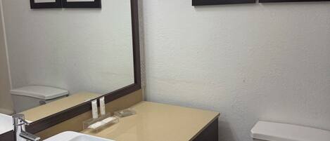 A bathroom with a white sink, mirror, and toilet. There are framed pictures on the wall.