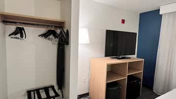 Ett hotellrum med en säng, ett skrivbord med en dator, en tv, en klädställning och ett litet bord.