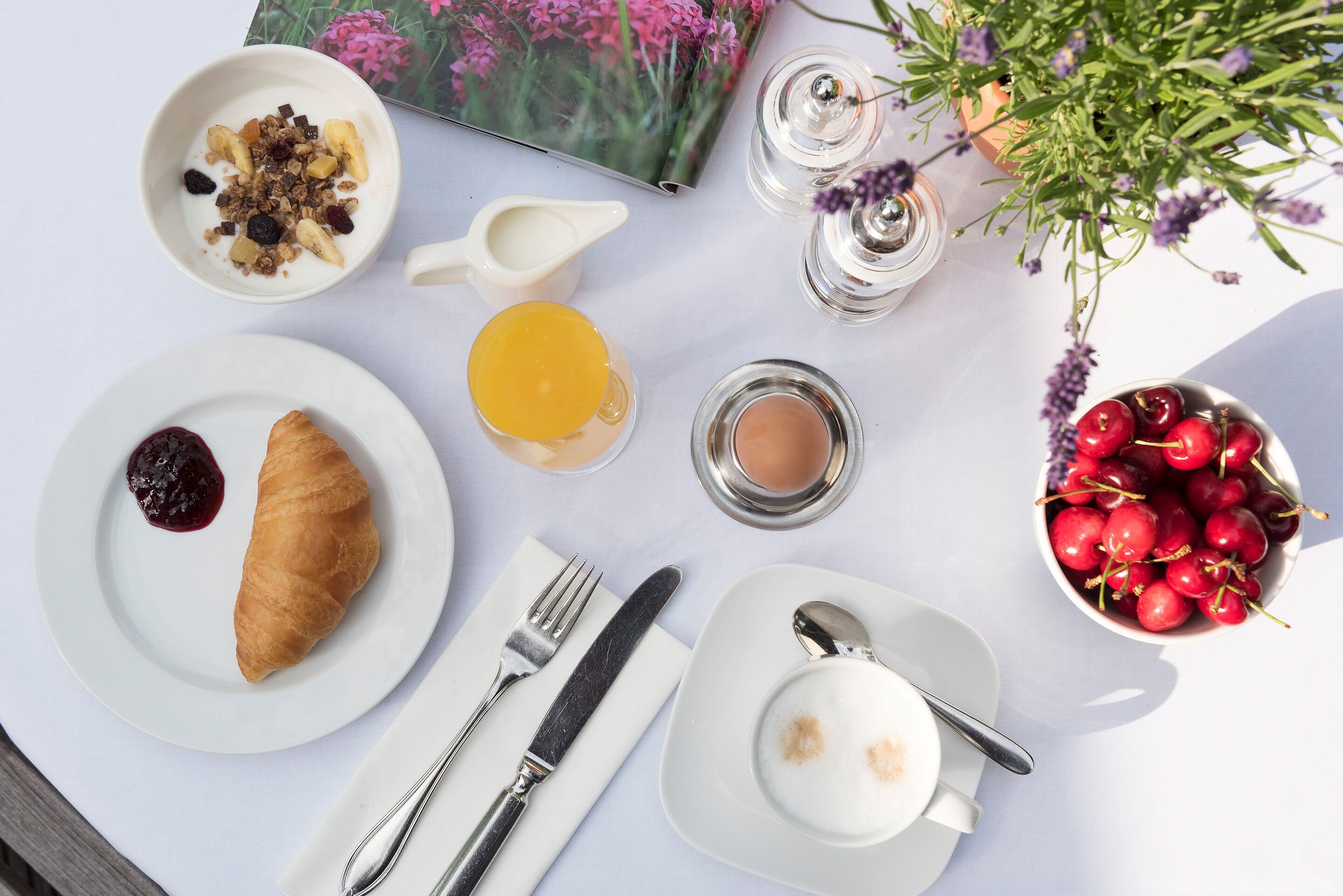 A breakfast setting with a croissant, fruit, and a bowl of cherries on a table.