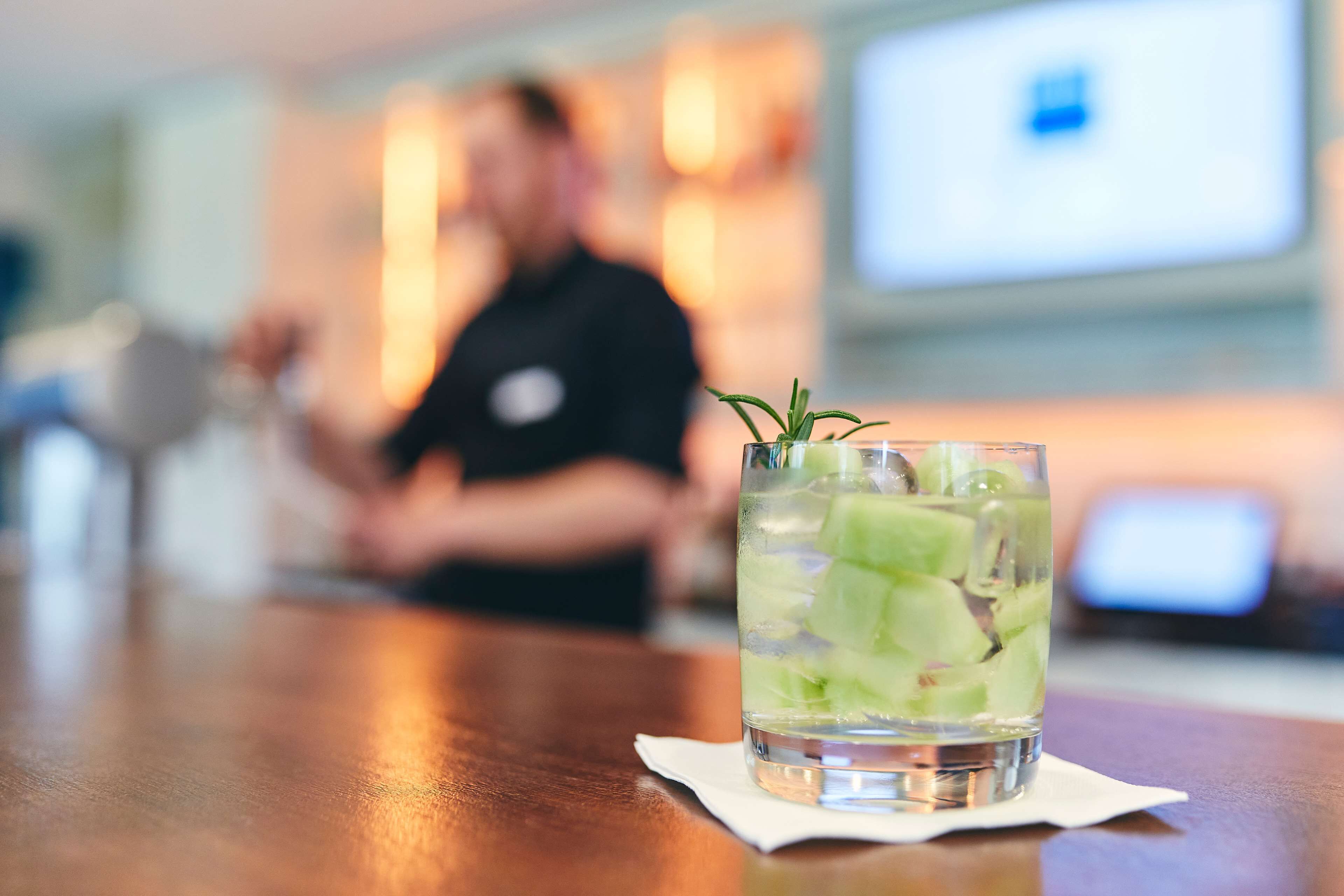 A glass of water with ice cubes and a sprig of rosemary on a wooden table.