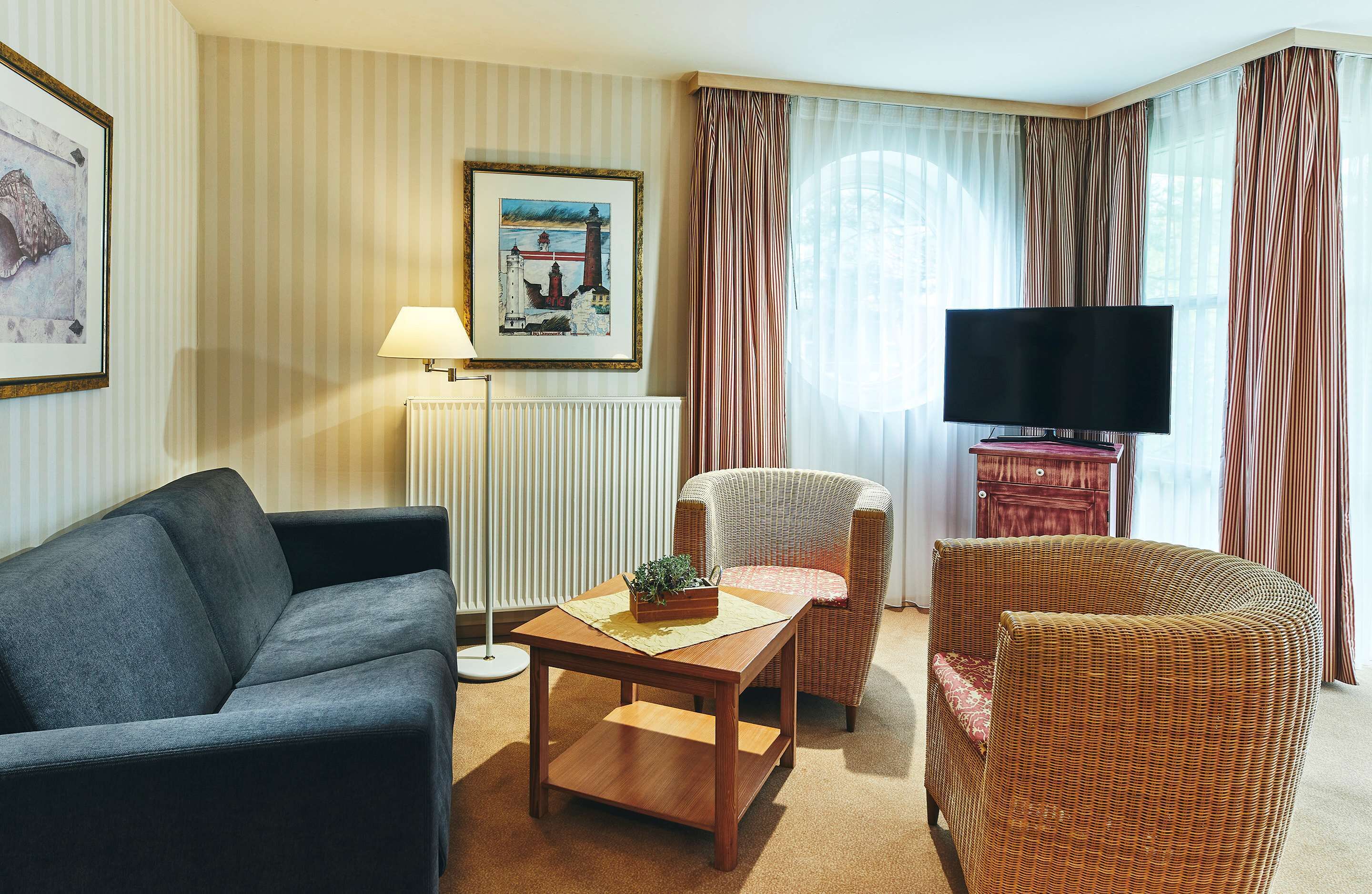 A living room with a sofa, armchair, and a table with a plant. There's a framed picture on the wall and a TV on a stand.
