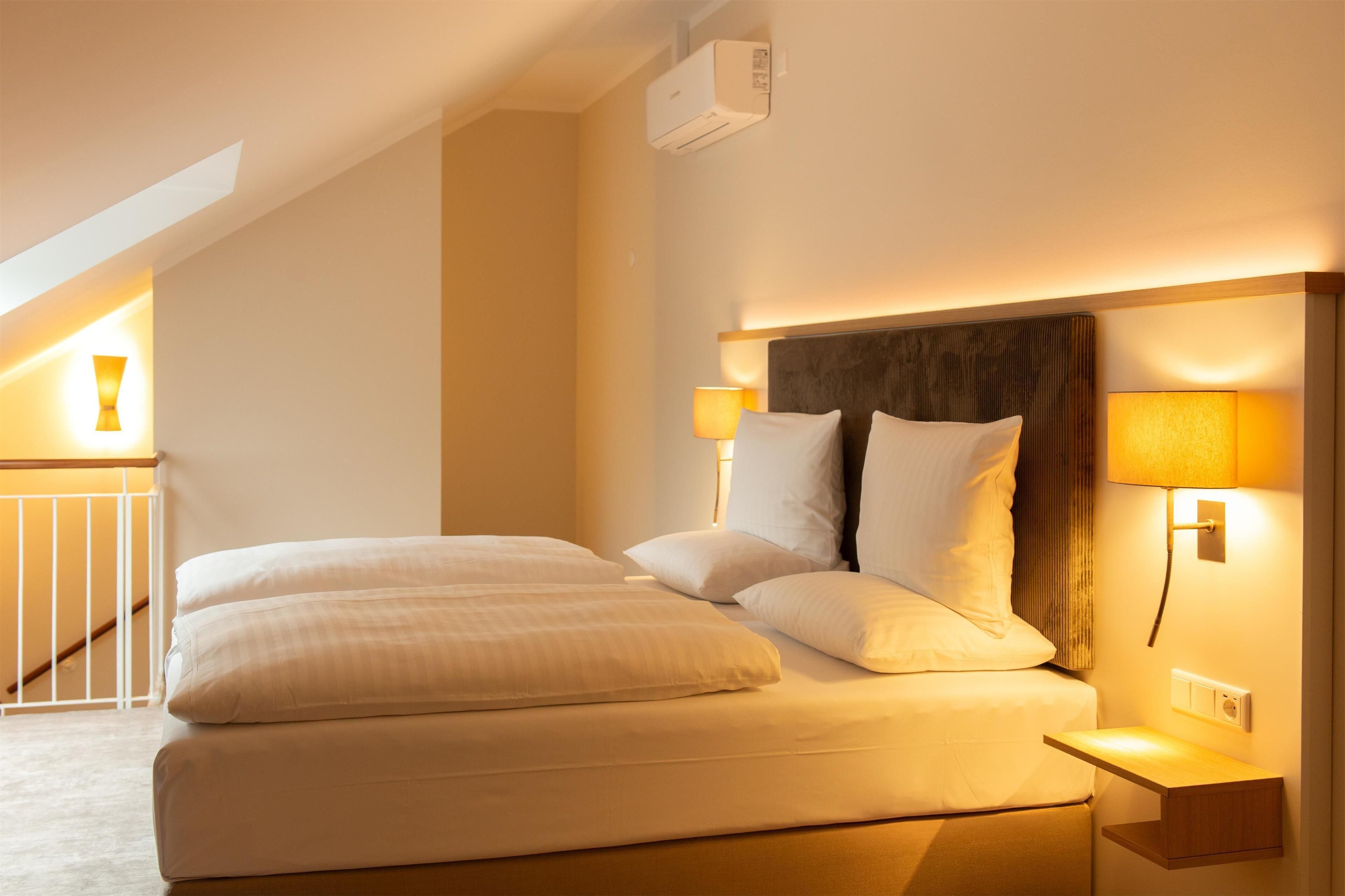 Une chambre d’hôtel avec un grand lit, deux lampes de chevet, une tête de lit en bois et un appareil de climatisation fixé au mur.
