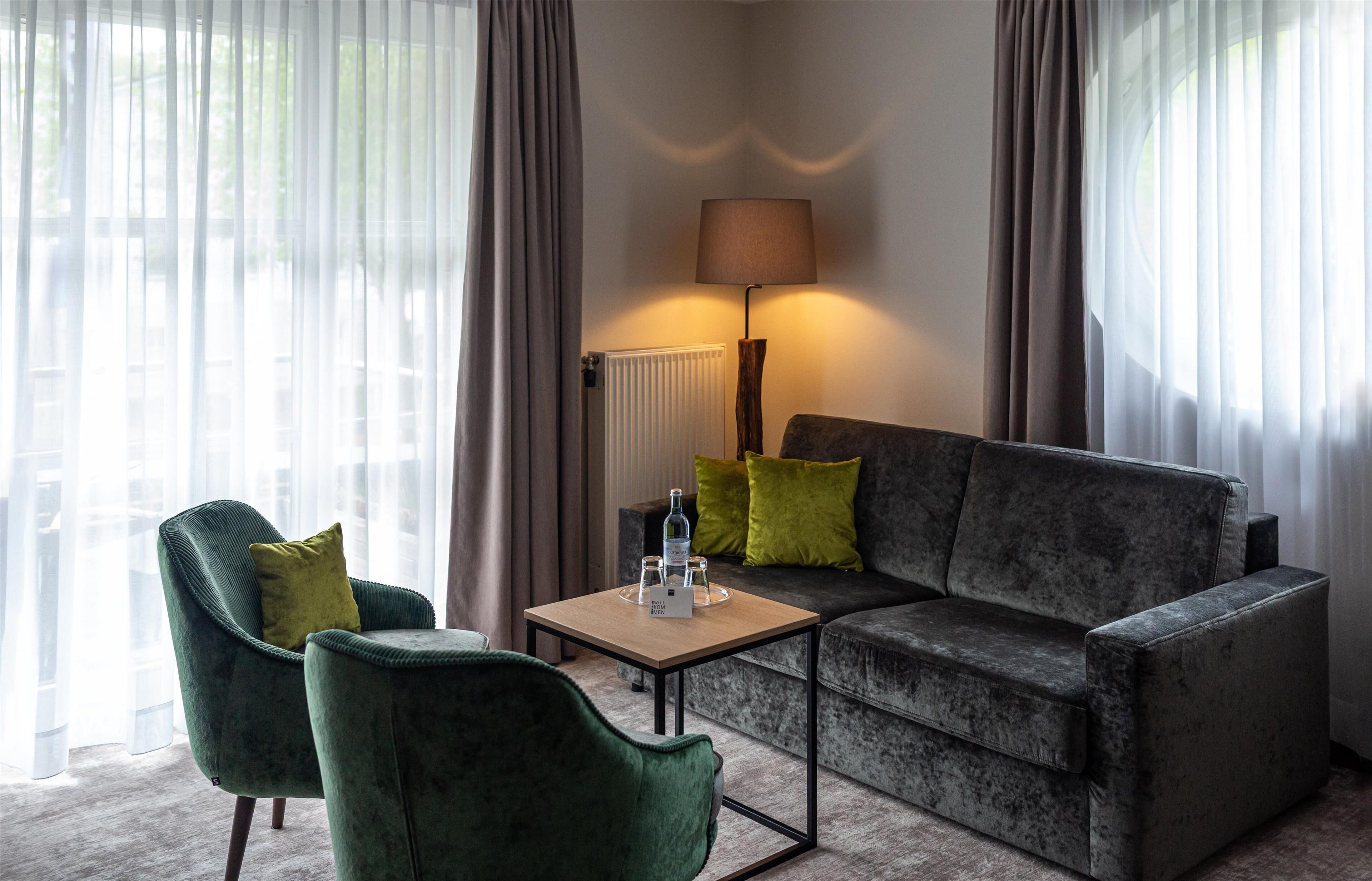 A modern living room with a grey sofa, two green armchairs, a wooden coffee table, and a floor lamp.