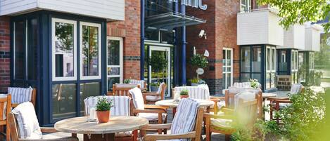 An outdoor seating area with wooden tables and chairs, a potted plant, and a building with a 'Dorint' sign.