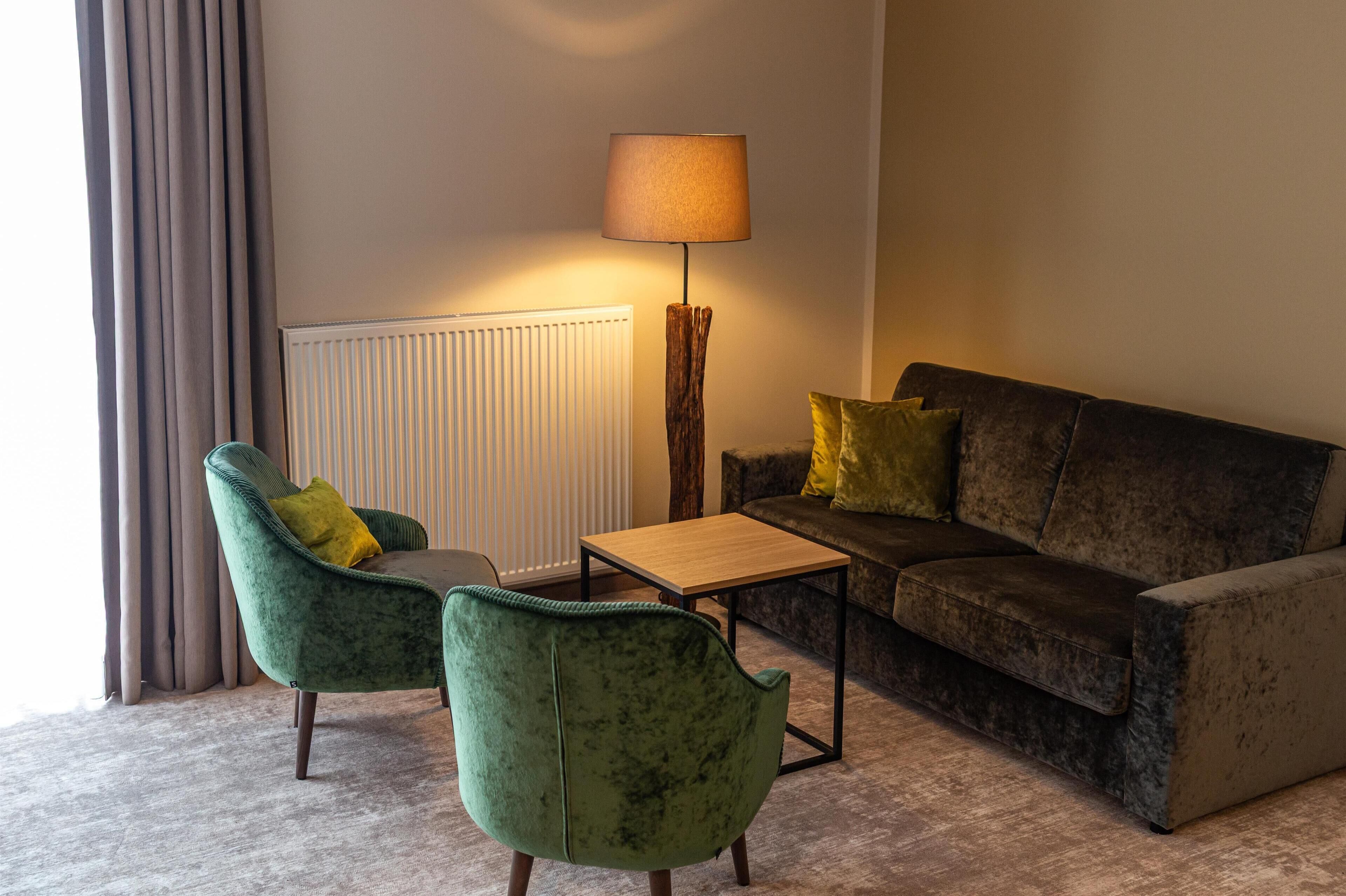 Una sala de estar acogedora con un sofá verde oscuro, dos sillones a juego, una mesa de centro de madera y una lámpara de pie.