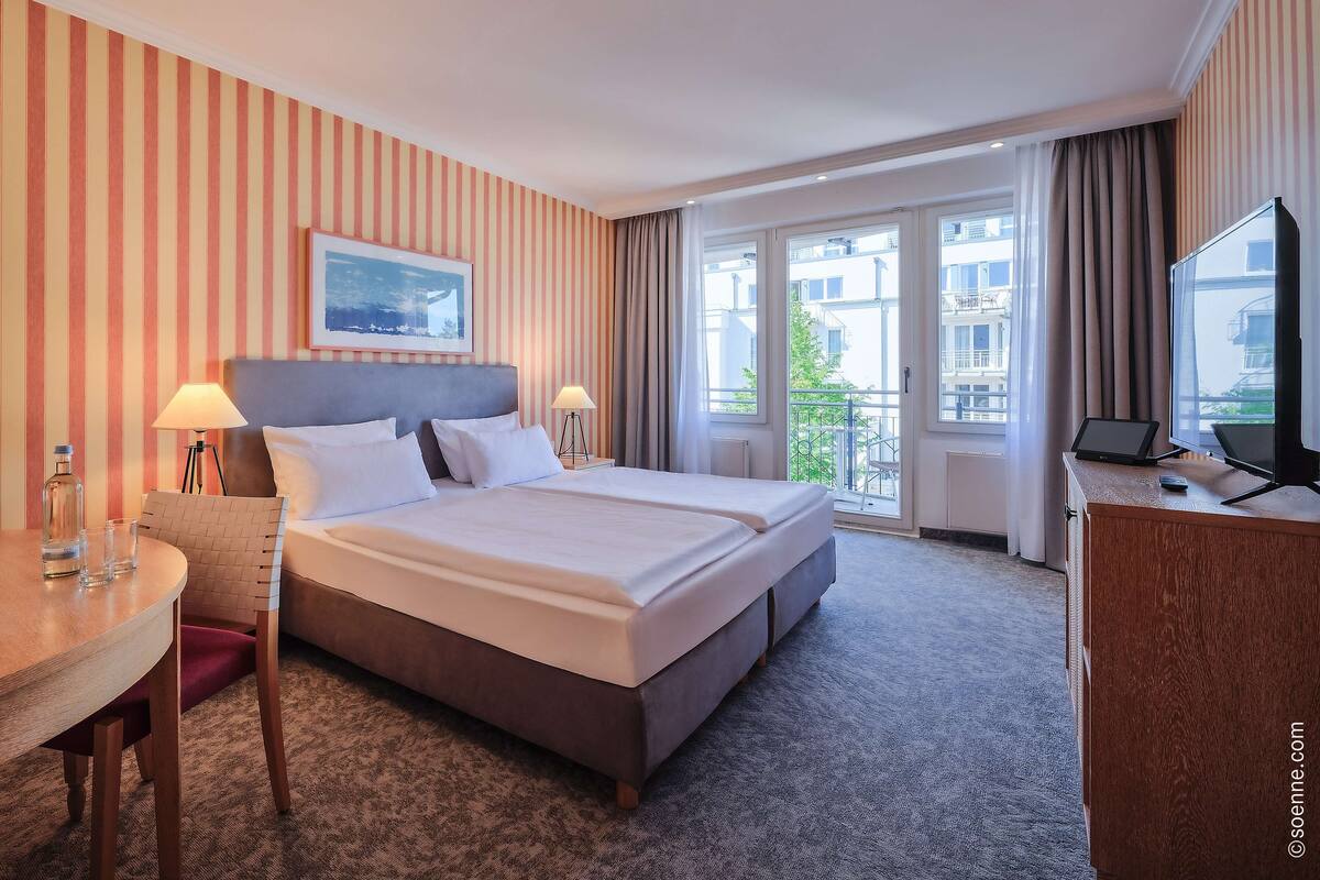 Ein Hotelzimmer mit einem großen Bett, einem Schreibtisch mit Stuhl, einem Fernseher und einem Fenster mit Blick auf Gebäude.