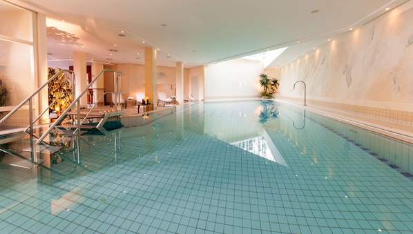 A large indoor swimming pool with tiled floors and walls, a glass railing, and a staircase leading to an upper level. - Dorint Strandhotel Binz/Rügen (Binz)