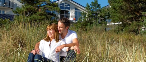 A couple sitting in tall grass with a house in the background.