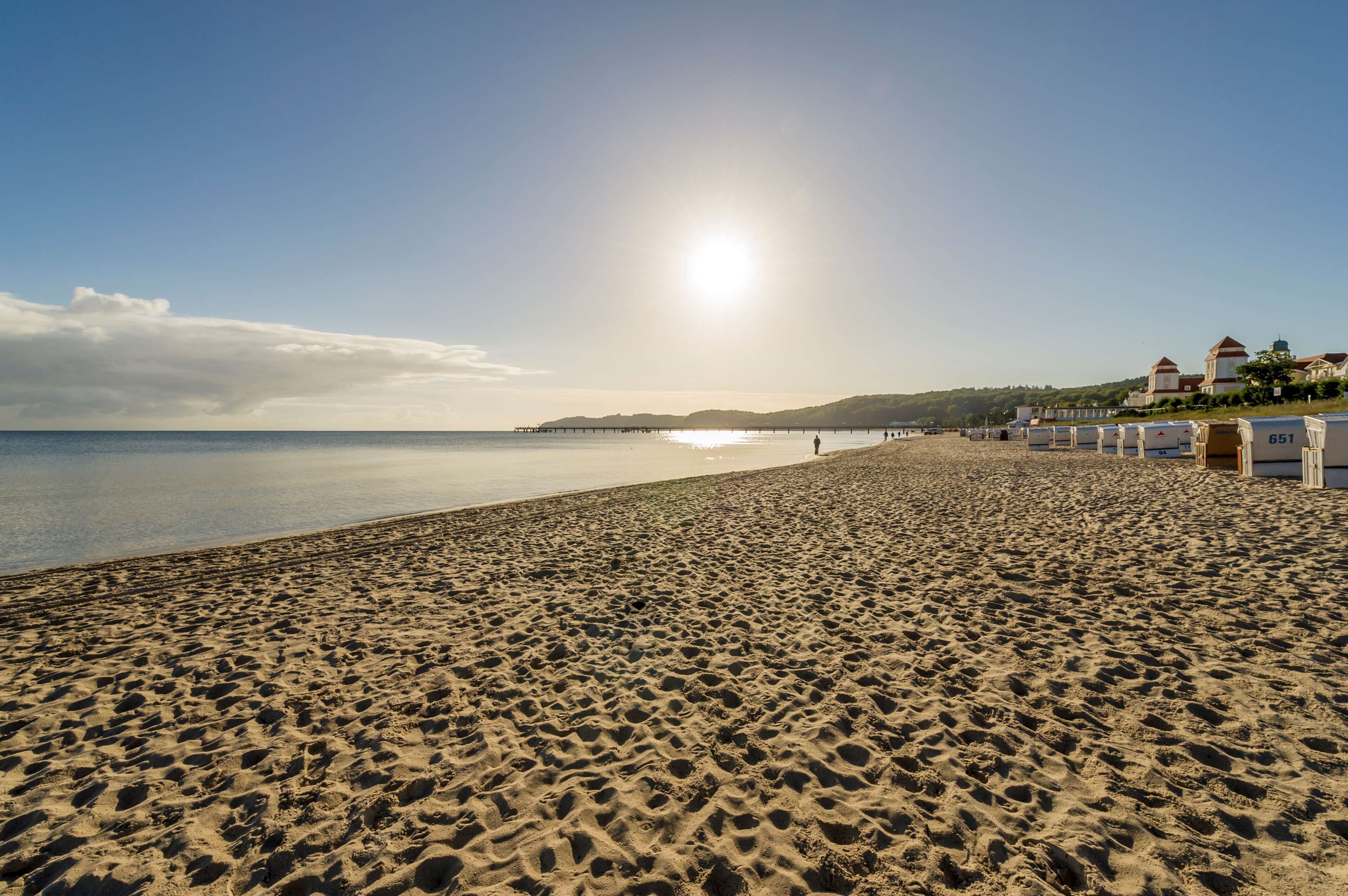 Une plage avec un ciel dégagé, une jetée au loin et des bâtiments portant des panneaux numérotés.
