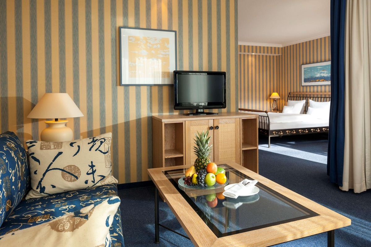 A hotel room with a television, a bed, a dining table with fruit, and a sofa.