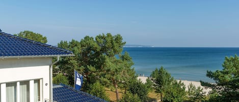 A coastal property with a balcony overlooking the sea, surrounded by trees.