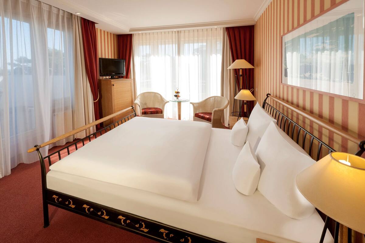 Ein Hotelzimmer mit einem großen Bett, einem Fernseher, einem kleinen Tisch mit Stühlen und einer Lampe.