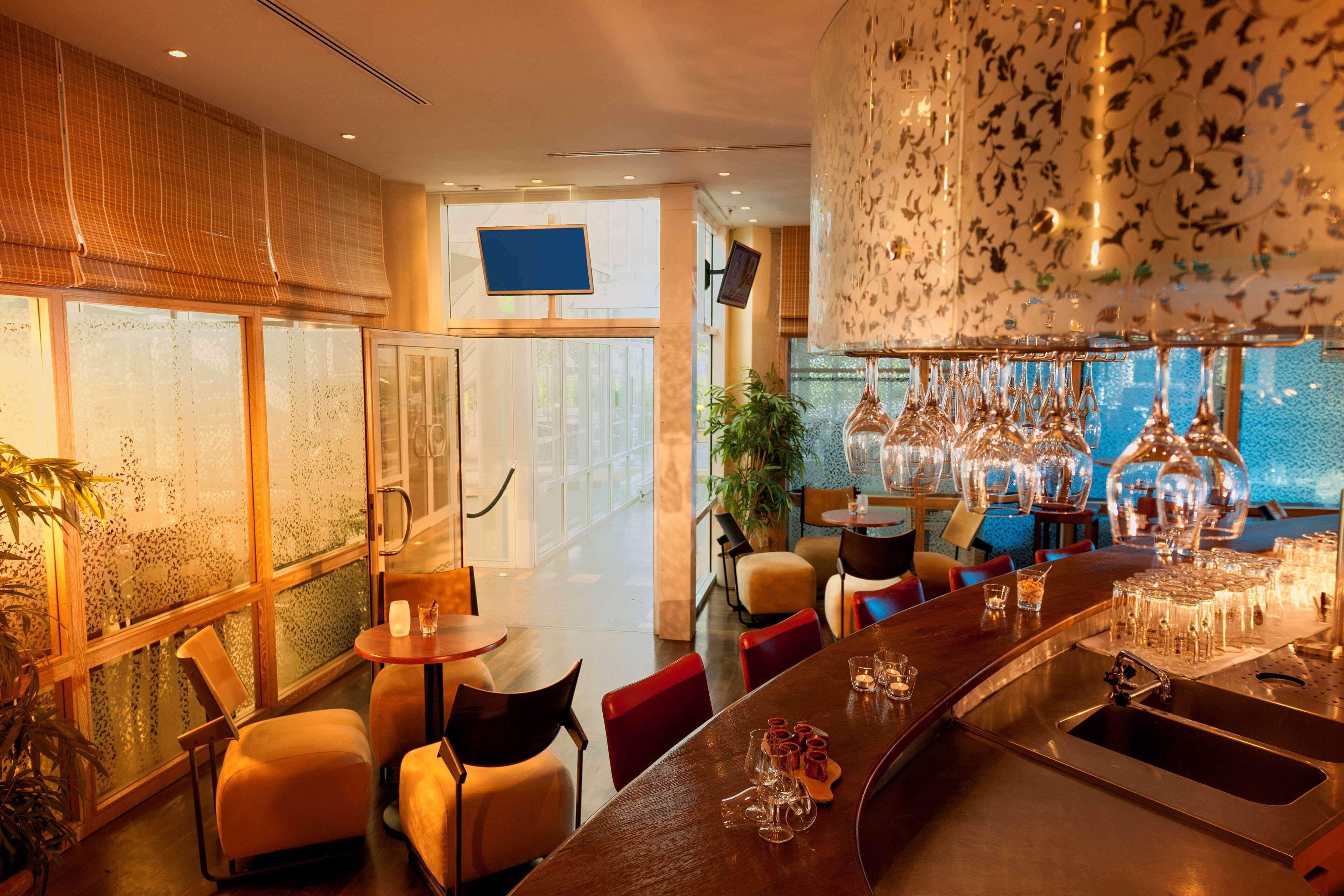 A modern bar area with seating, a large chandelier, and a view of the outdoors.