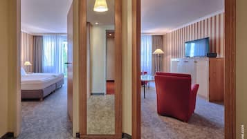 Una habitación de hotel con una cama, un sillón rojo, un televisor y un área de comedor con mesa y sillas.