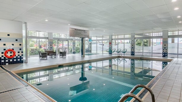 An indoor swimming pool with clear glass walls, a lifebuoy on the wall, and a sign with rules. - Super 8 by Wyndham Macleod Trail Calgary (Calgary)