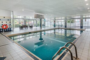 Una piscina interior con paredes de vidrio transparente, un flotador en la pared y un cartel con normas.