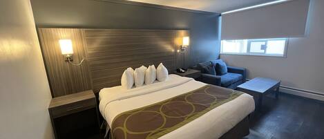 A hotel room with a large bed, a bedside table, a desk, a chair, and a window.