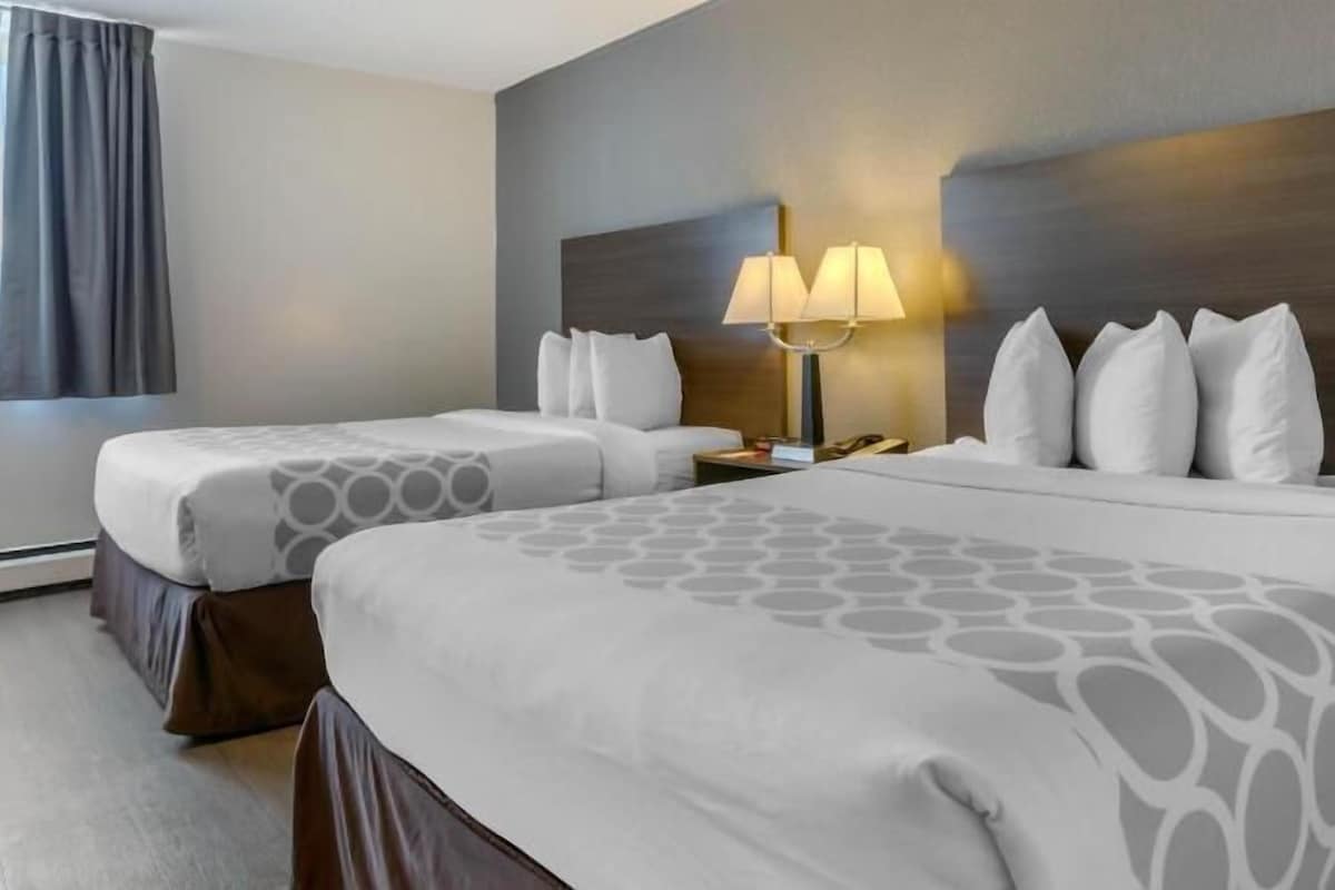 A hotel room with two beds, a nightstand with a lamp, and a large window with curtains.