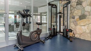 A gym with an exercise bike, a multi-functional weight machine, and a stone wall. - Super 8 by Wyndham Macleod Trail Calgary (Calgary)