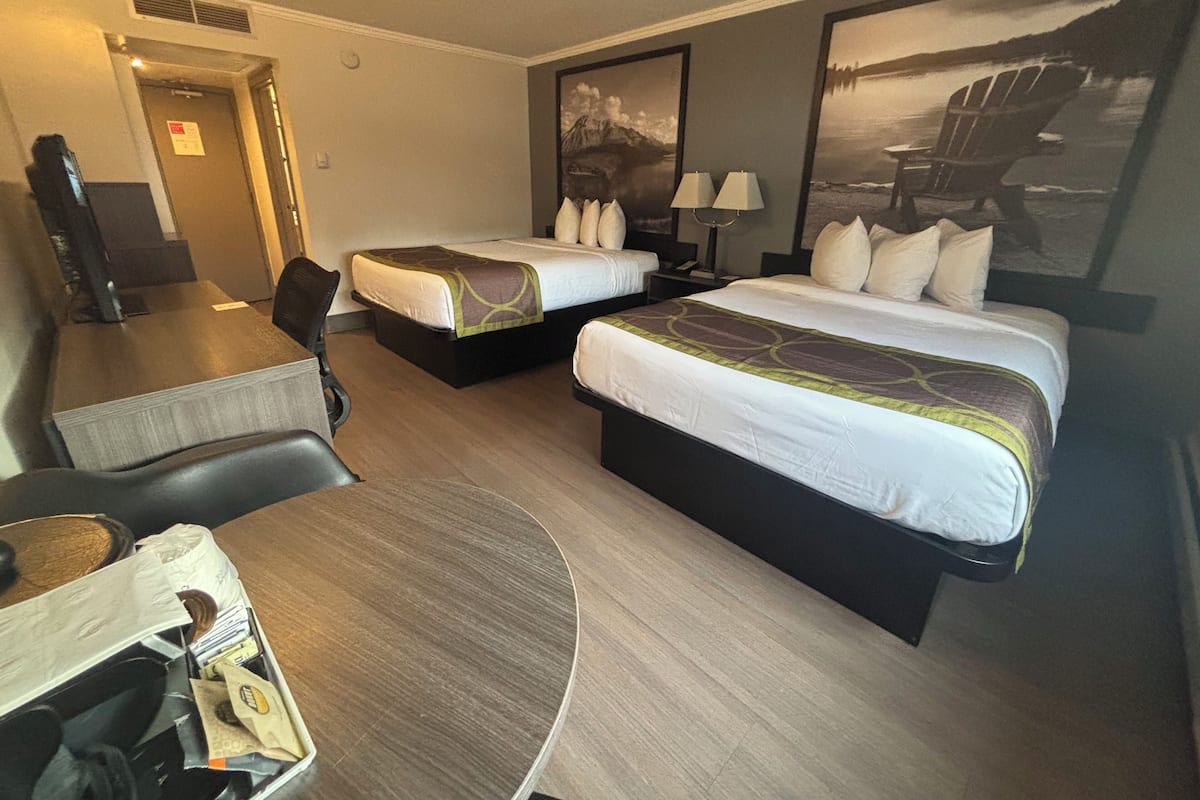 Quarto de hotel com duas camas, uma escrivaninha, uma cadeira e uma janela grande com vista para um lago.