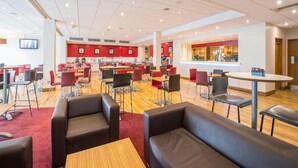 A spacious indoor area with multiple seating arrangements, including tables and chairs, and a bar area with a counter. - Travelodge London Docklands (London)