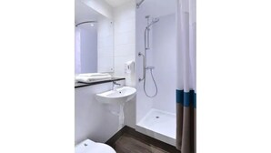 A modern bathroom with a sink, mirror, shower, and toilet. - Travelodge London Docklands (London)