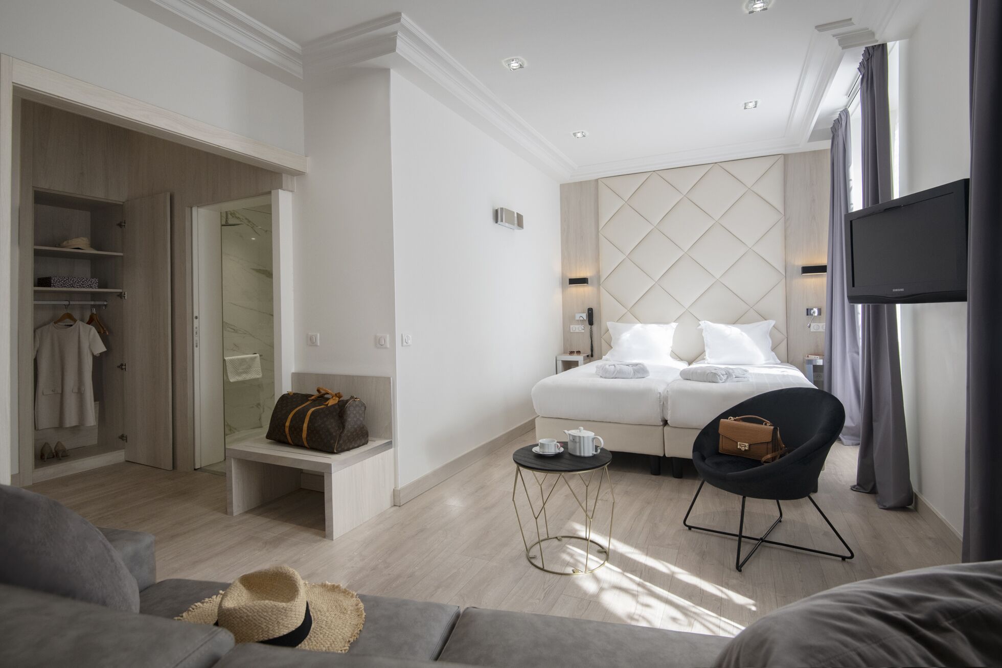 A modern hotel room with a bed, a seating area, a TV, and a closet.