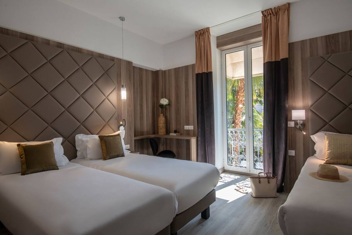 Habitación de hotel con dos camas, un escritorio y vistas al exterior.