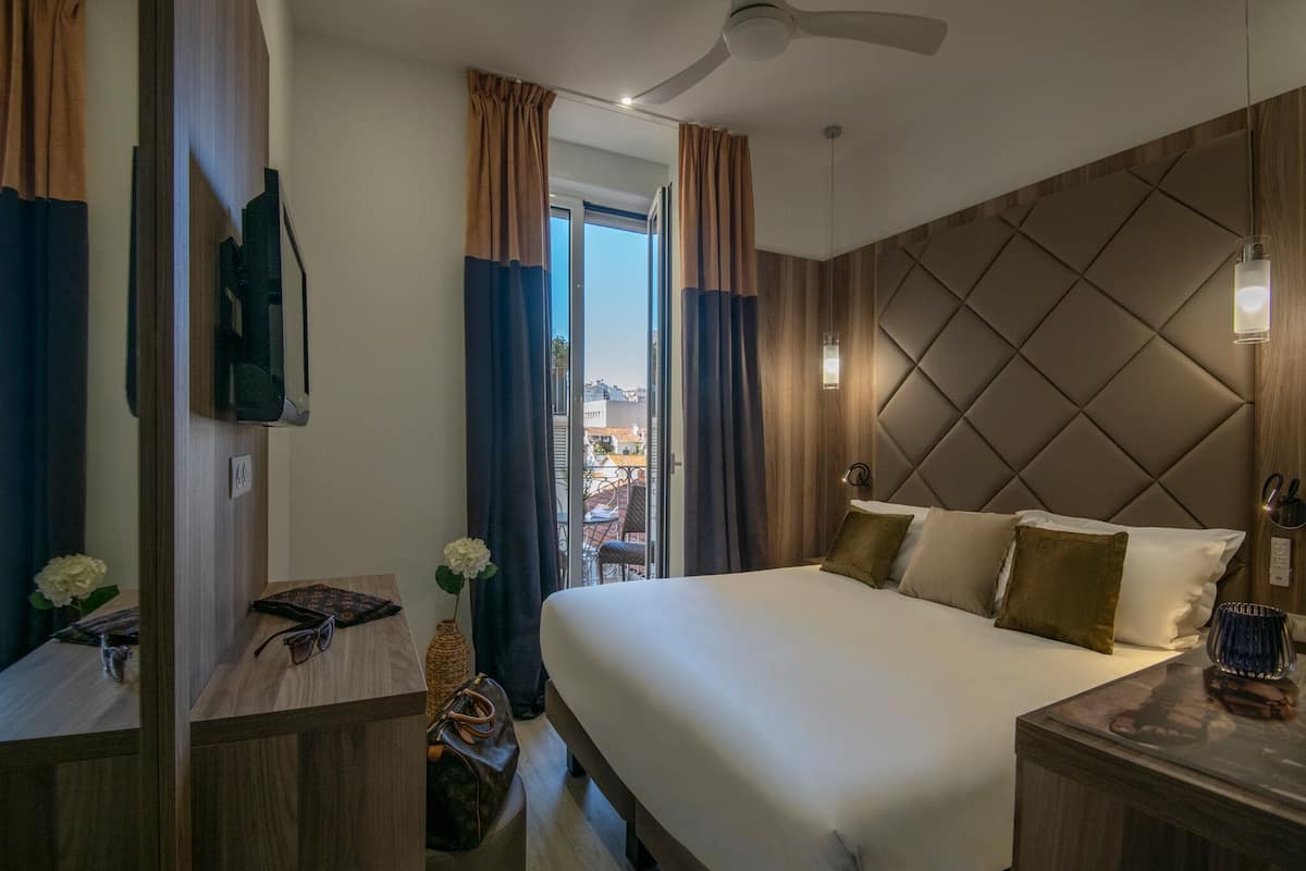 Una habitación de hotel moderna con una cama grande, un televisor de pantalla plana en la pared y vistas a la ciudad a través de la ventana.