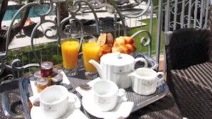 A breakfast tray with cups, a teapot, and orange juice on a balcony overlooking a pool and palm trees. - Golden Tulip Cannes hotel de Paris (Cannes)