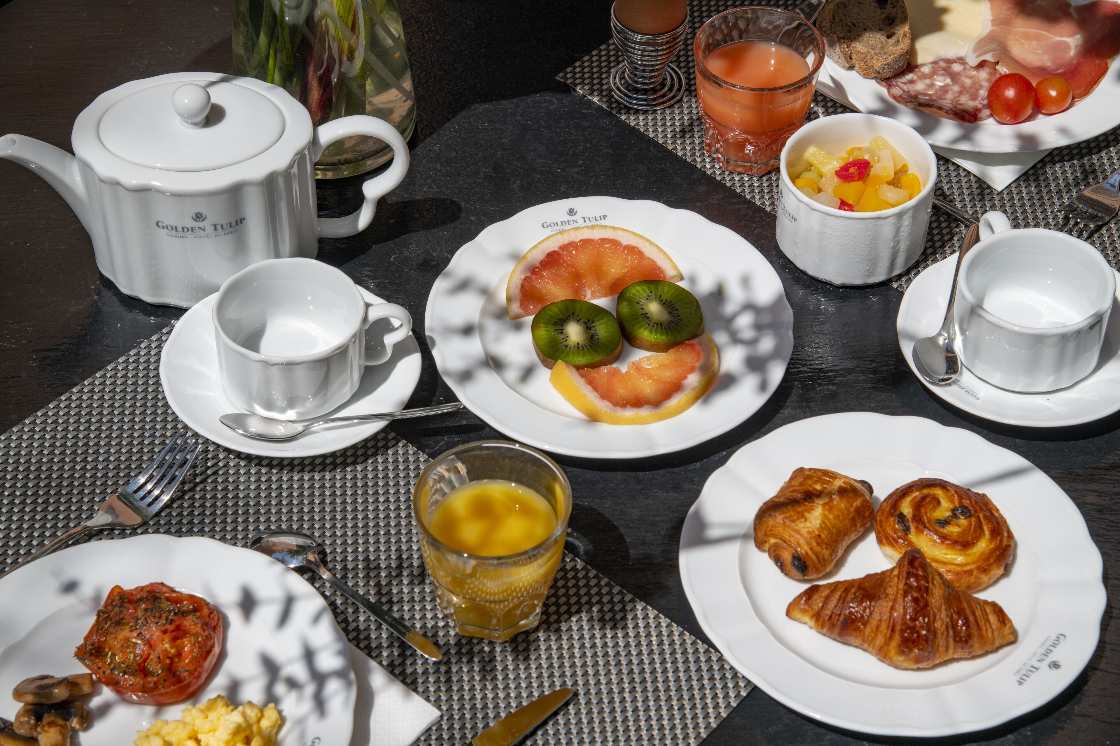 A table set with breakfast items including croissants, fruit, and a teapot.