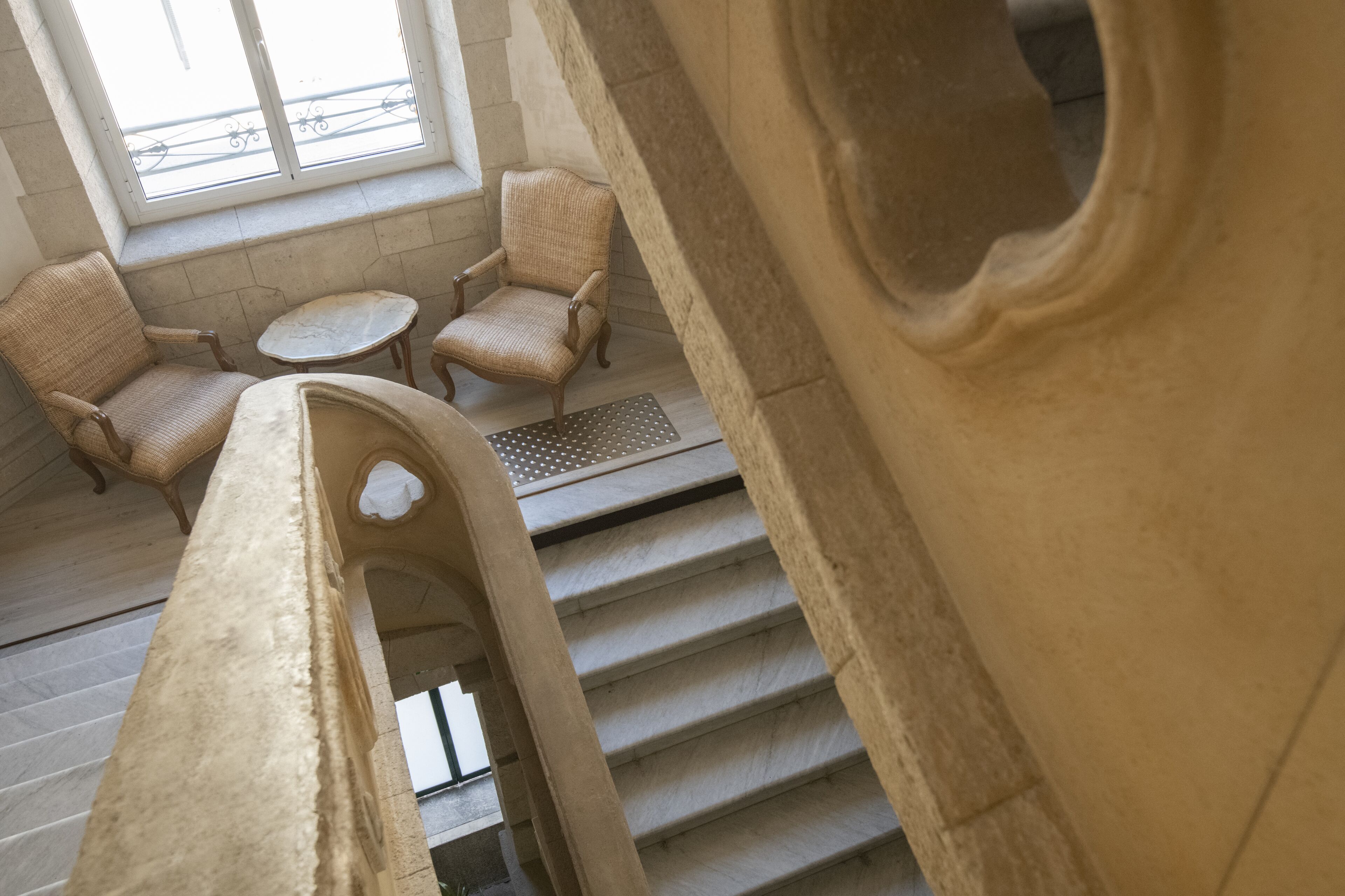 A staircase with a view of a seating area with two wicker chairs and a small table.