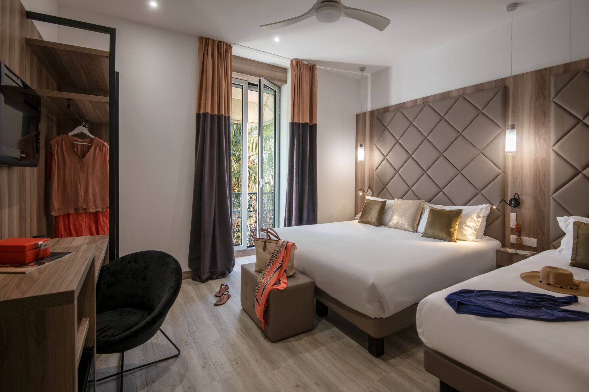 Ein modernes Hotelzimmer mit zwei Betten, einem Schreibtisch, einem Sessel und einem Kleiderschrank.