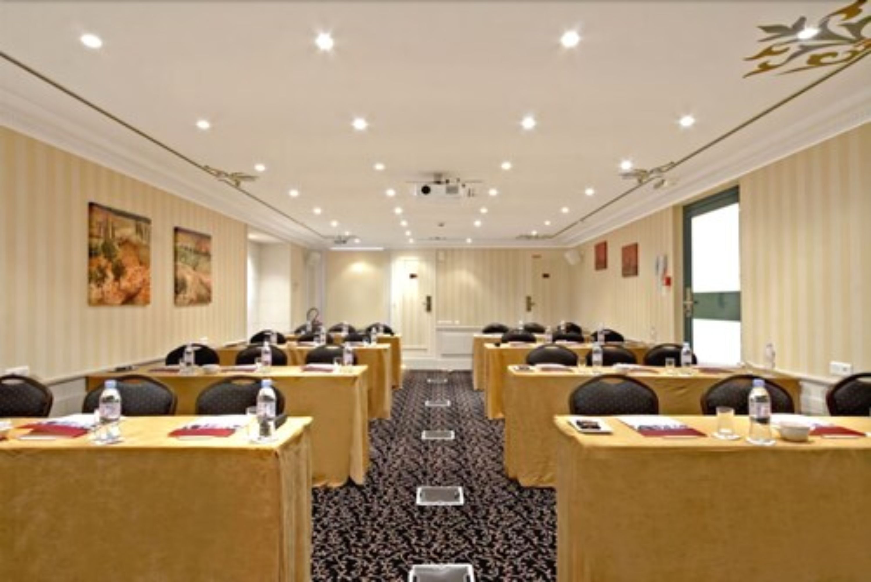 Een congreszaal met rijen tafels, stoelen en een projectiescherm.