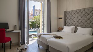 A hotel room with a large bed, a desk with a TV, a red chair, and a view of a pool and buildings outside. - Golden Tulip Cannes hotel de Paris (Cannes)