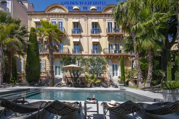 Un hotel con piscina, sillas de descanso y palmeras.