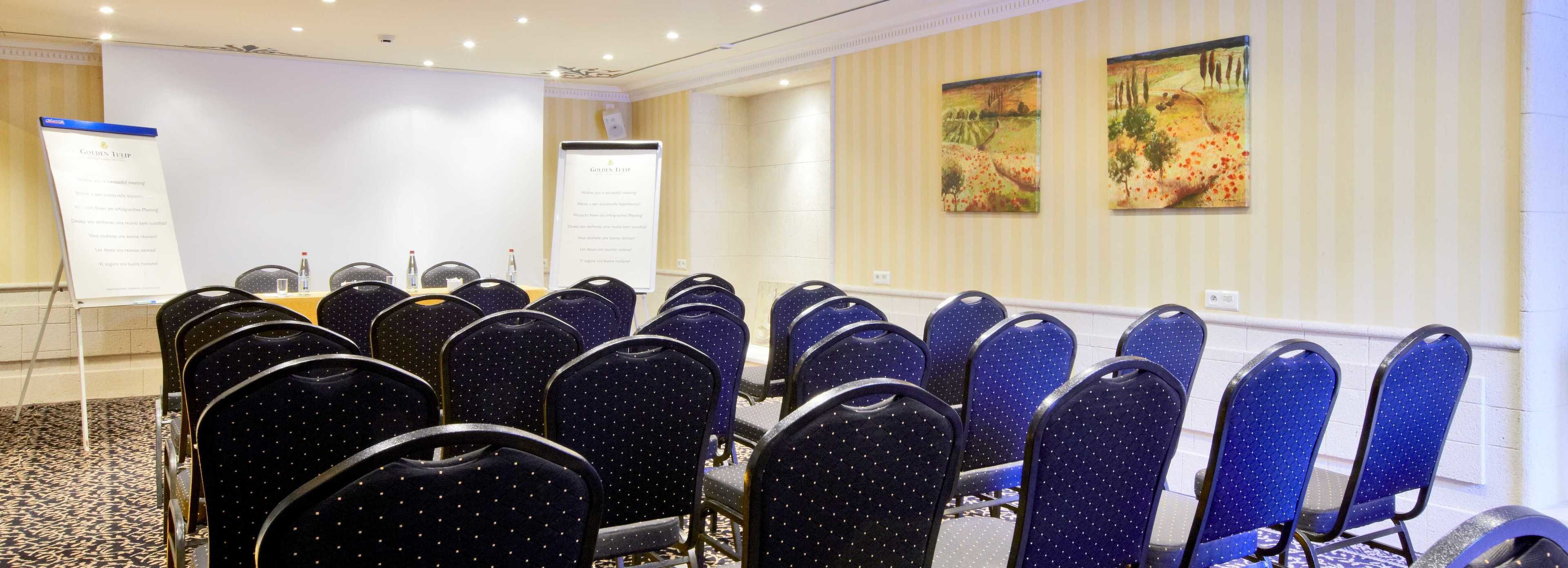 A conference room with rows of blue chairs, a whiteboard, and two paintings on the wall.