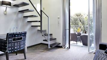 A modern hotel room with a desk, chair, and a staircase leading to a balcony.