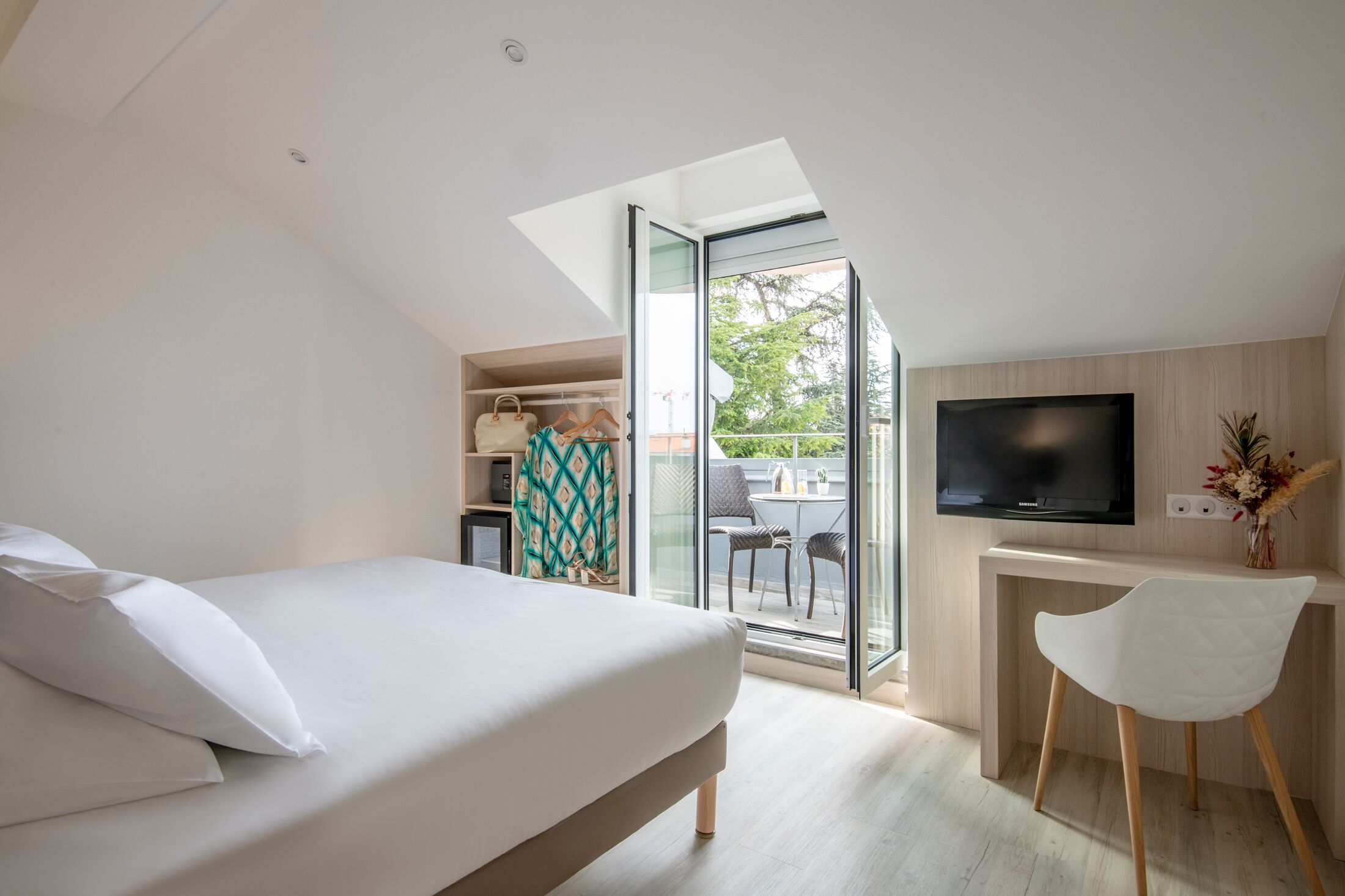 Un dormitorio moderno con cama, escritorio y televisor, y vista al exterior.